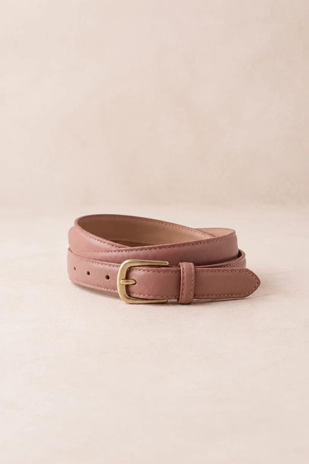 Dusty rose waist belt with a matte gold-tone buckle, loosely coiled